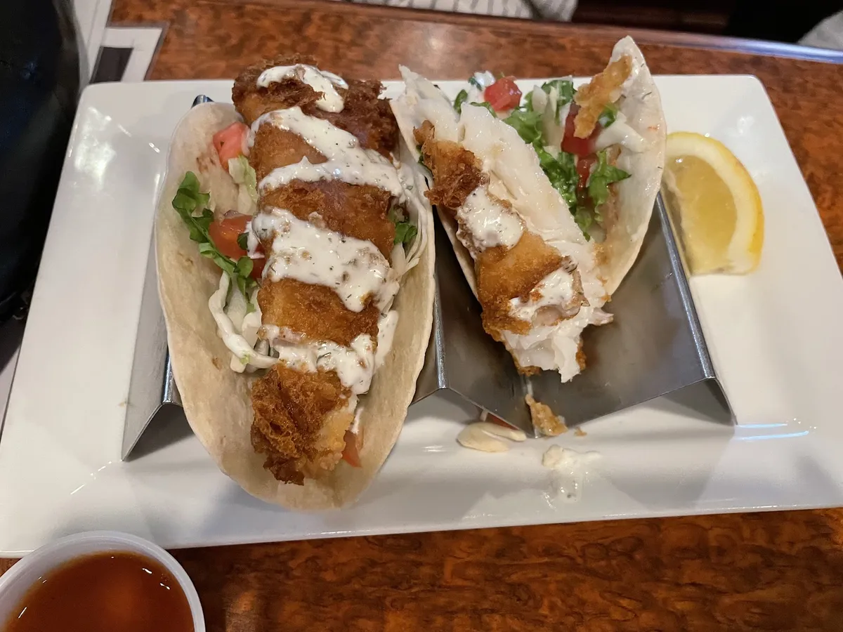 Two fish tacos with sauce and a lemon wedge
